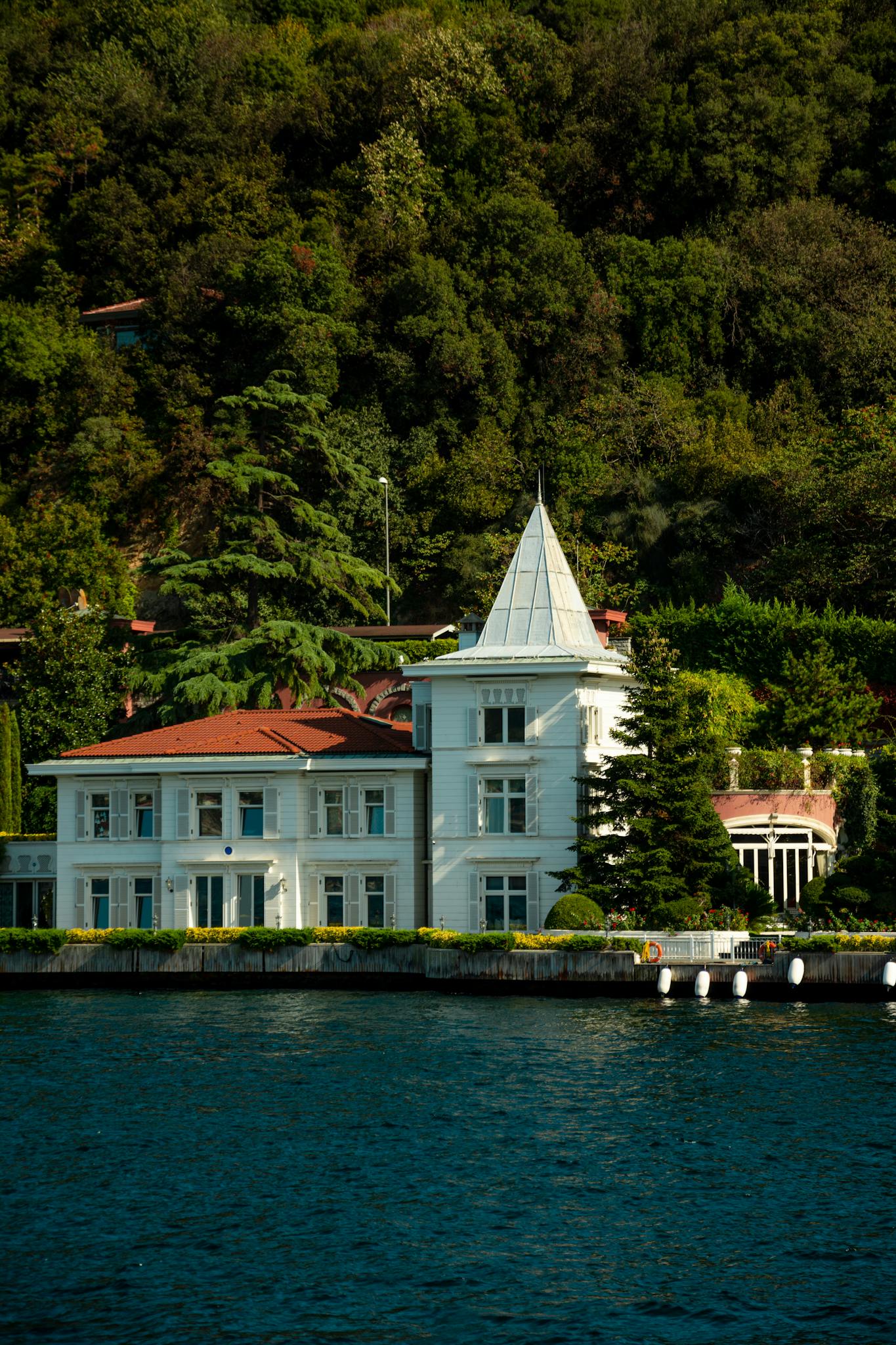 Beautiful white mansion by the water surrounded by lush greenery.