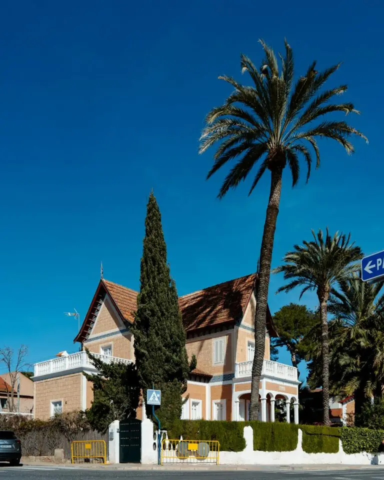 Elegant villa surrounded by palm trees under a bright blue sky in Santiago de la Ribera, Spain.