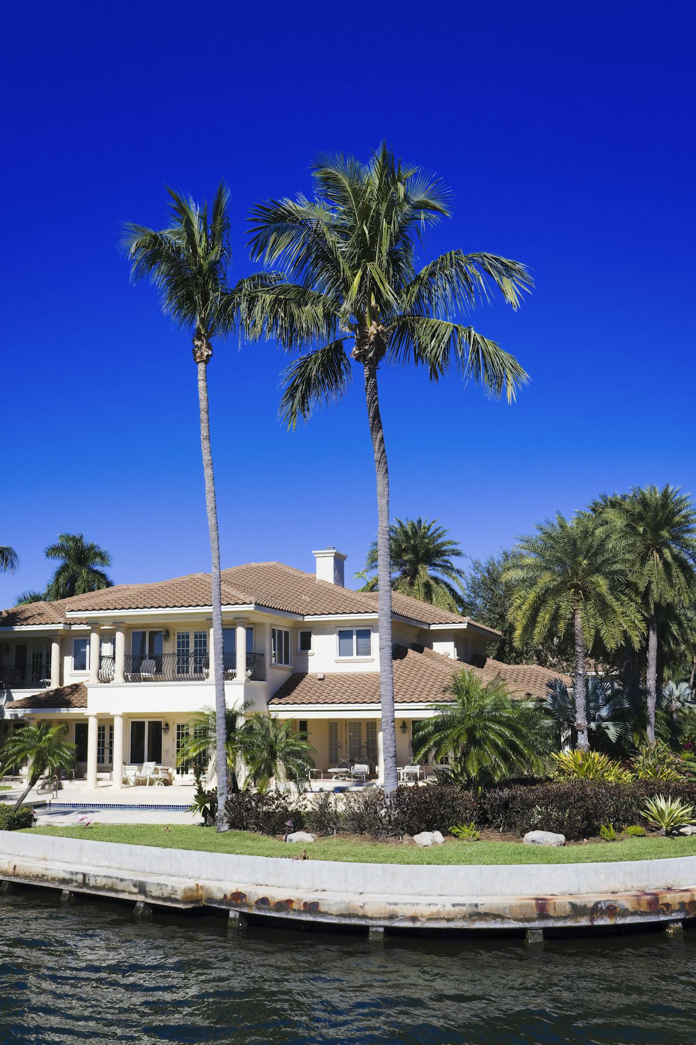 Stunning waterfront home bordered by palm trees under a bright summer sky.
